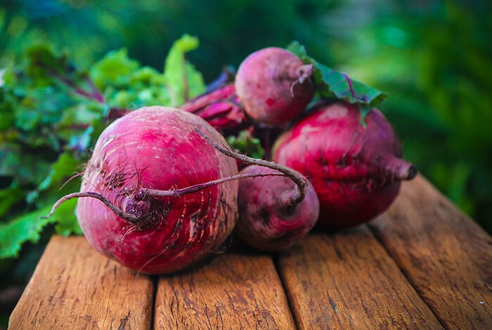 Raw beets on a wooden chopping board.