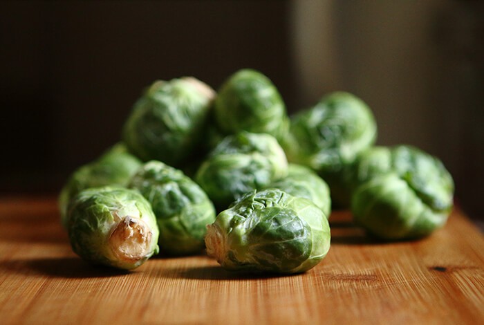 Raw brussel sprouts on a wooden chopping board.