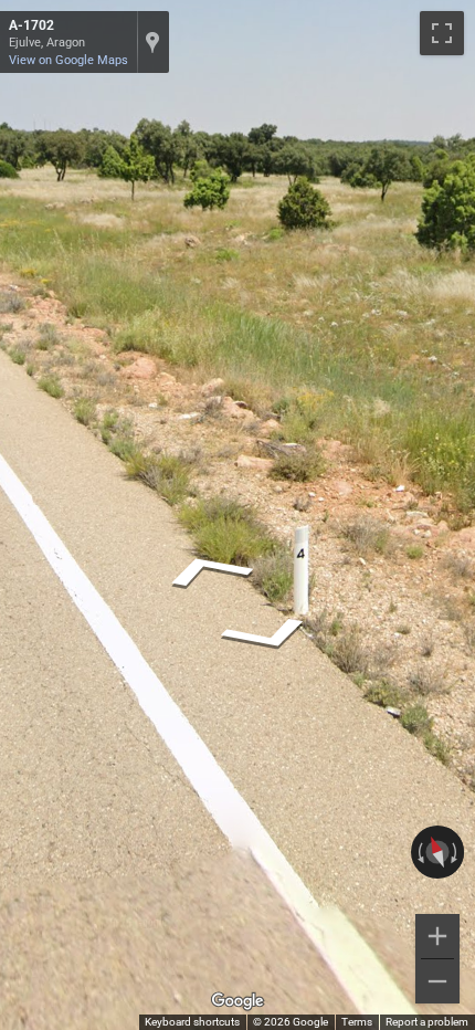Aragonese bollard, short and white, sometimes with black numbers or a yellow painted top, standing on a roadside.