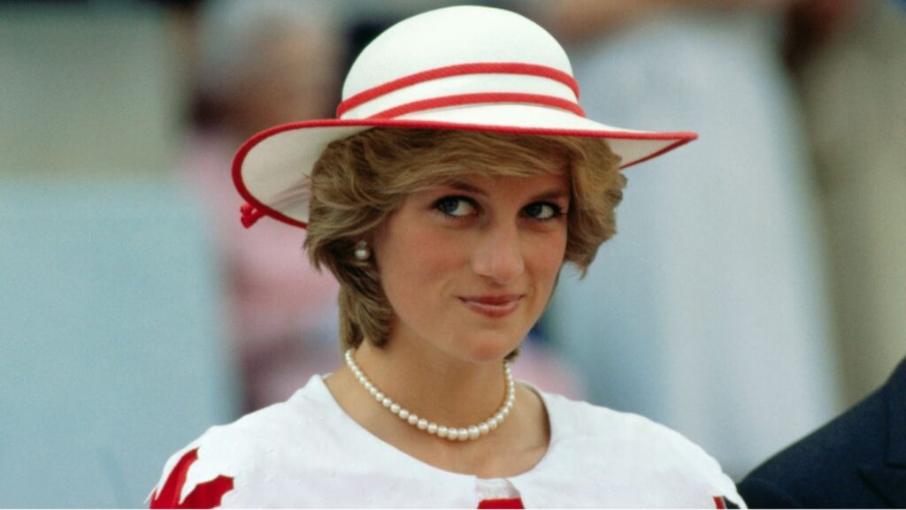 A photo of Princess Diana wearing a white dress with red accents, complemented by a wide-brimmed white hat with a red ribbon. She is adorned with a pearl necklace and matching earrings