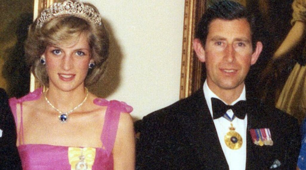 Princess Diana and the then Prince Charles at a state event. Diana is wearing a pink dress with the Spencer Family Tiara, alongside a pair of sapphire earrings with a matching necklace. Charles is wearing a black suit with a white collar shirt and bow tie and some medals. There are some paintings hung up behind them in gold frames.