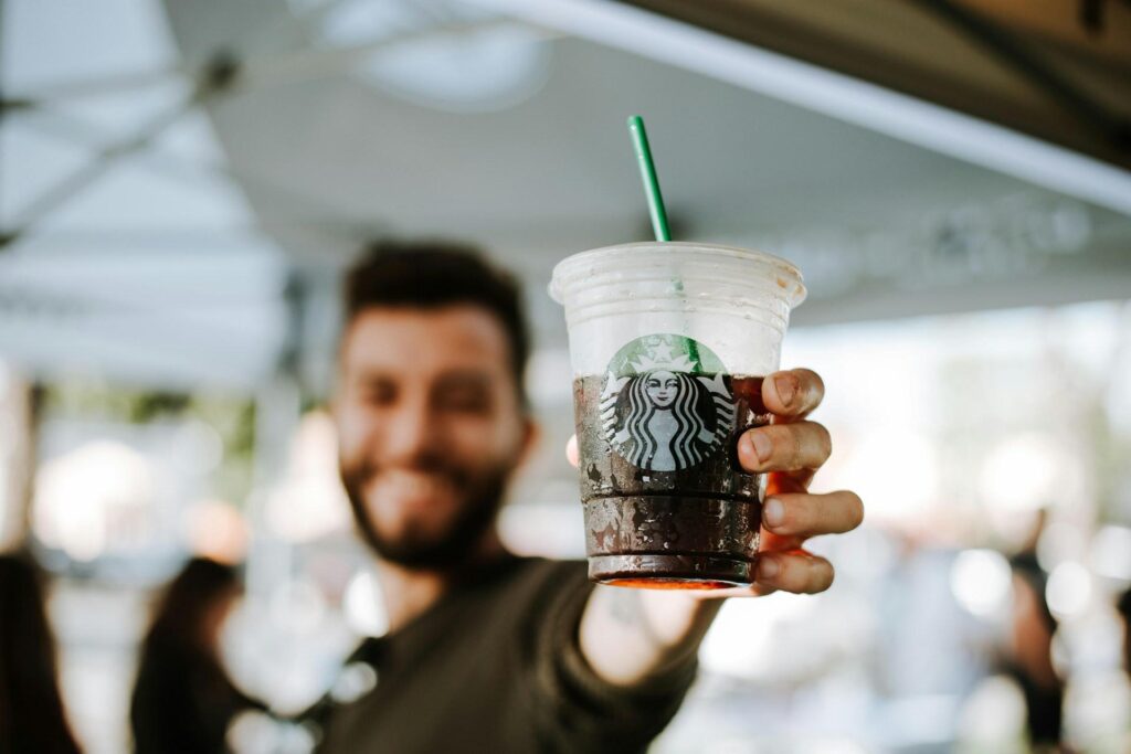 A man holding a Starbucks plastic cup with straw filled with iced coffee