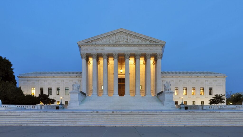 The U.S. Supreme Court building seen in the evening with its lights on.