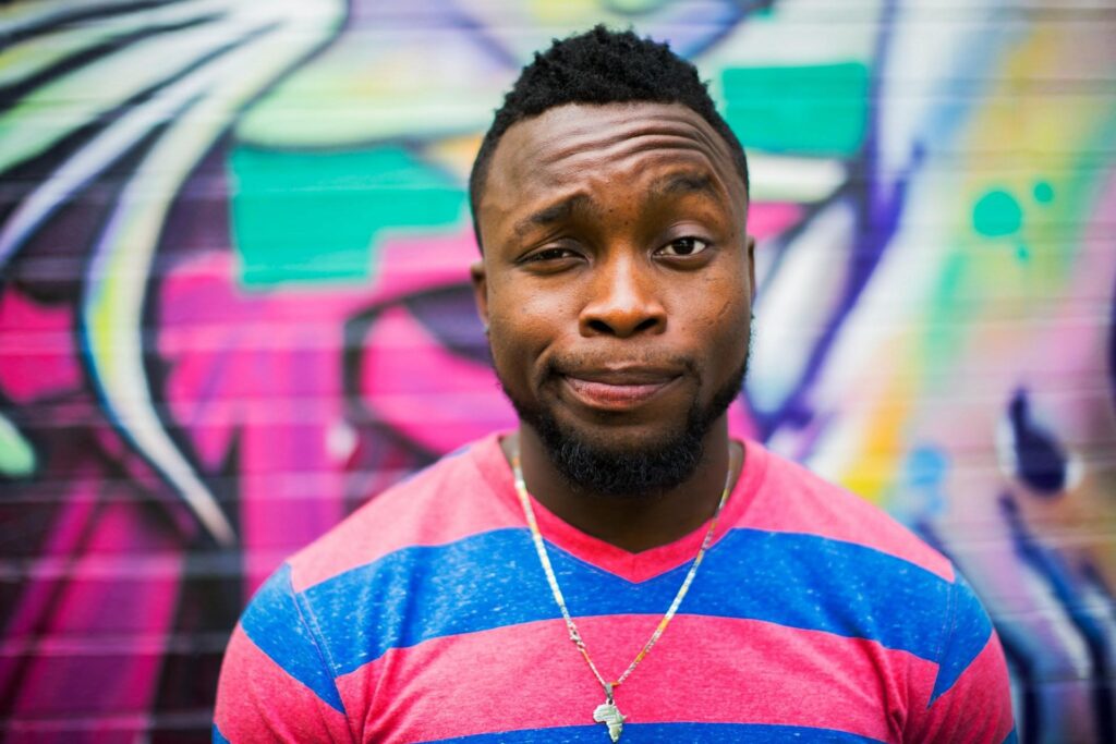 A black man wearing striped red and blue T-shirt making a face