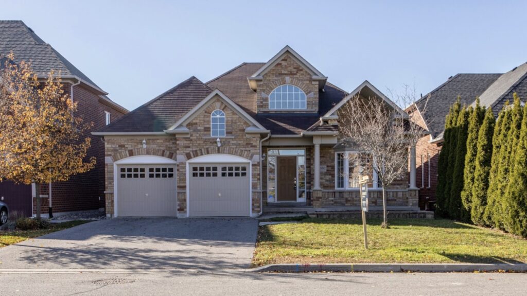 A brick house sits on a manicured lawn with fall trees in the yard