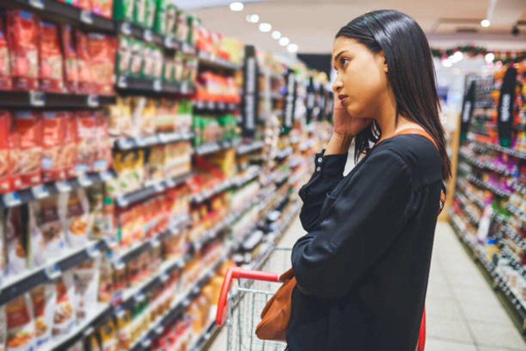 A woman looks discouraged as she checks prices at the grocery store