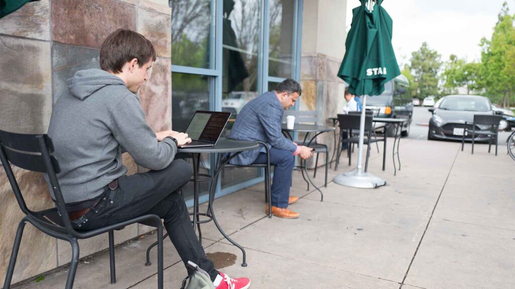 A young, millennial age male tech worker in a hoodie sits outdoors and works on a laptop near the Googleplex, headquarters of Google Inc in the Silicon Valley town of Mountain View, California.