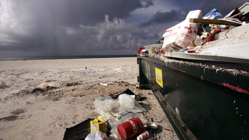 Trash on a Florida beach and in a garbage can seen in the daytime.