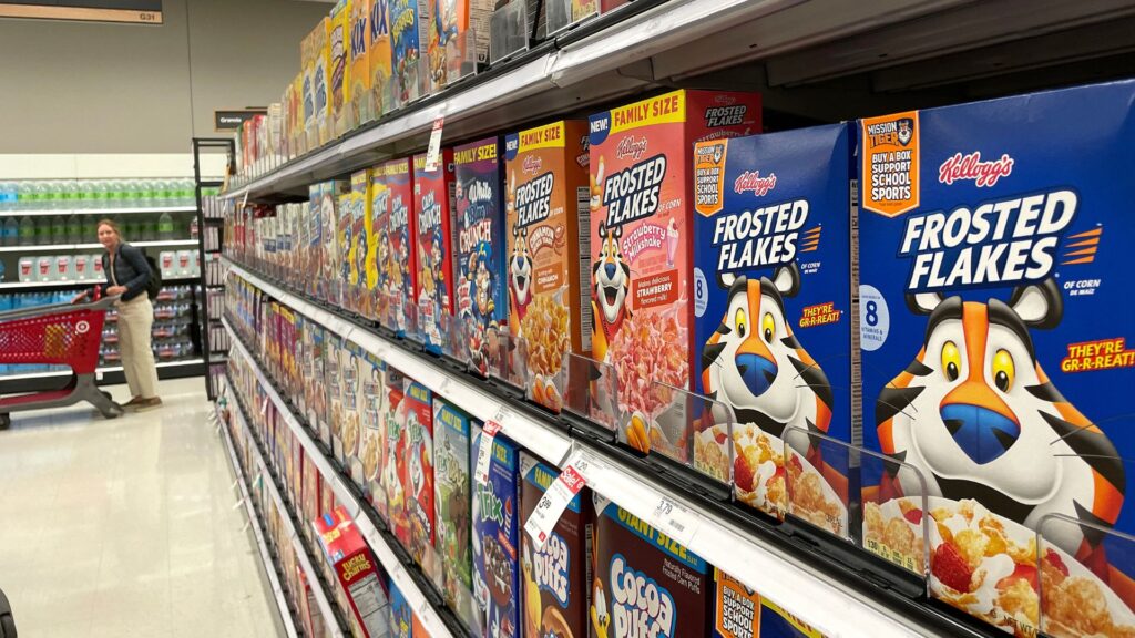 A close-up of cereal options on Target store shelves, with a customer and a cart in the aisle.