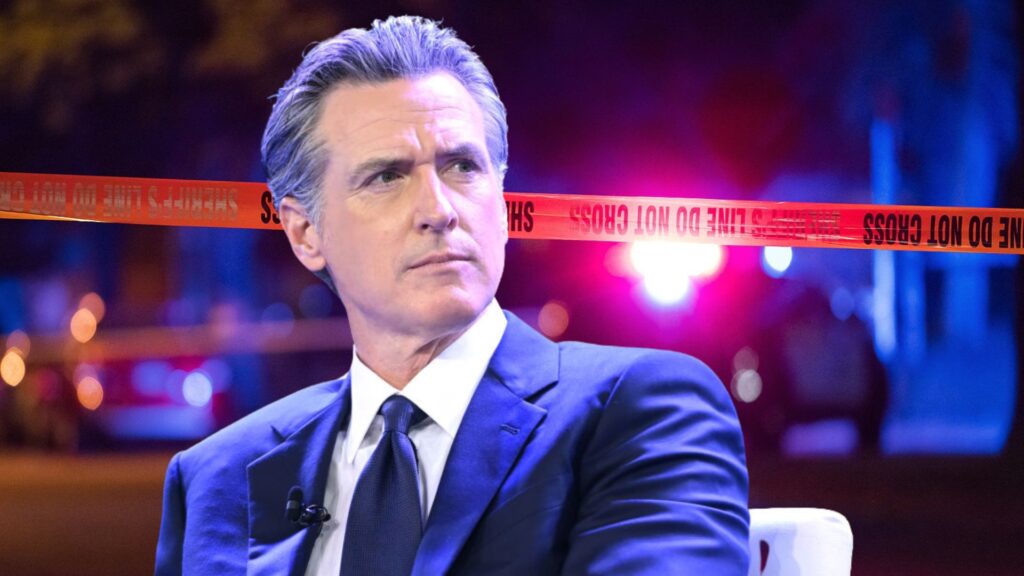 Governor Gavin Newsom speaking at a public event, looking focused with a blurred background featuring police tape