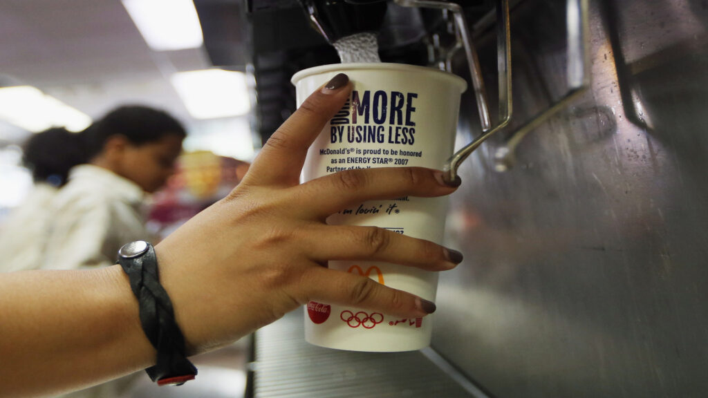 A person holds a McDonald's cup up to a self-serve drinks machine.