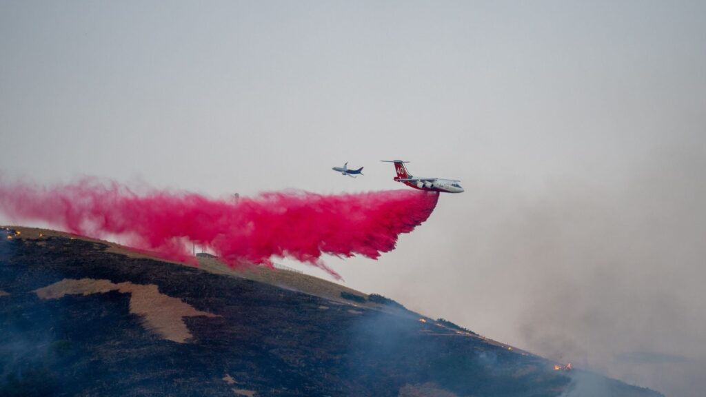 An airplane disperses a large plume of red fire retardant over a hillside near Salt Lake City to combat a wildfire