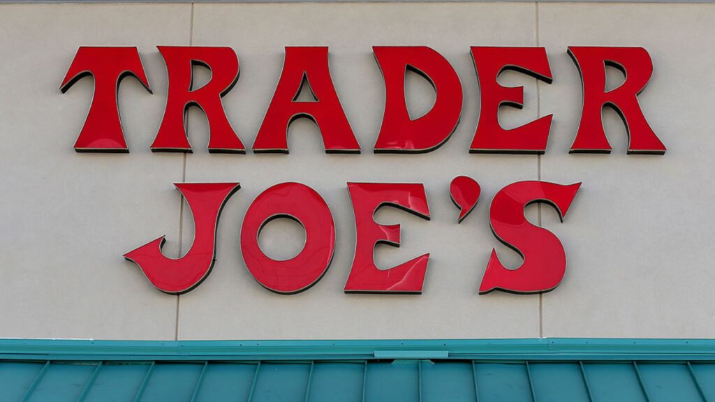 A close-up of the red 'Trader Joe's' signage on a store, featuring bold, stylized letters against a beige building façade