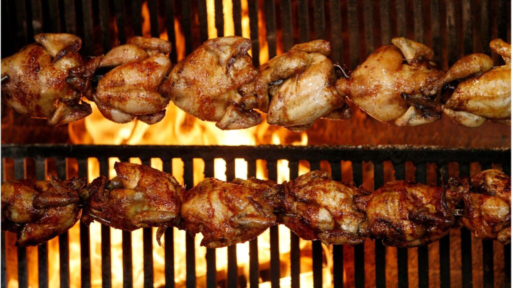 Rotisserie chickens burning on top of a grill.