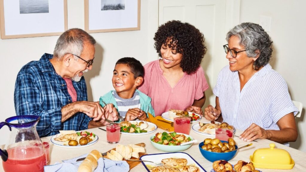 A multigenerational family enjoying a meal together at a dining table, smiling and interacting with each other, featuring a diverse group with adults and a child