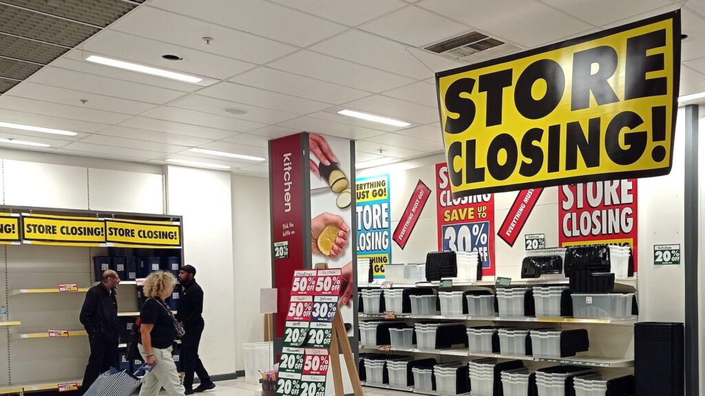 A retail store displaying multiple "Store Closing" signs with various discounts, as customers browse through the remaining merchandise