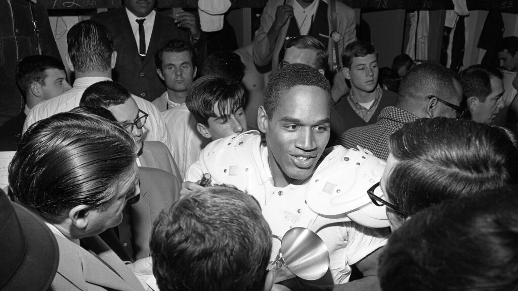 A gray scale image of OJ Simpson talking to reporters; OJ Simpson Dies at 76 After His Battle with Prostate Cancer