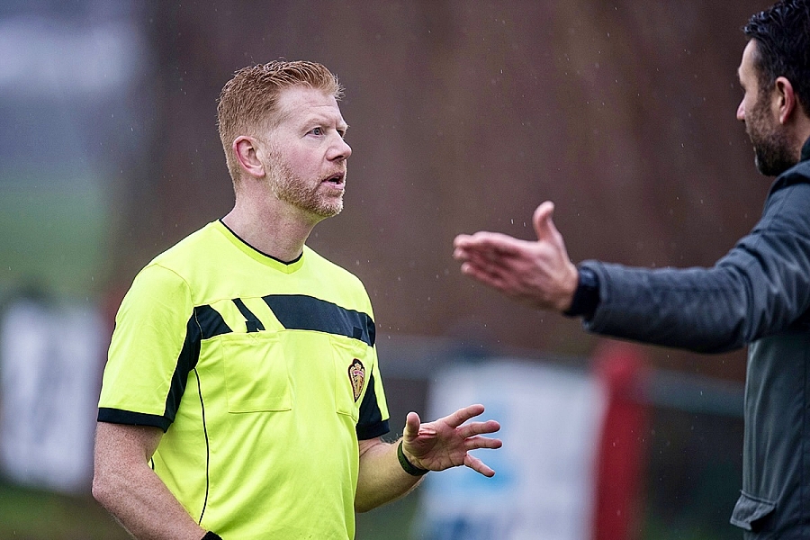 Een voetbaltrainer valt de scheidsrechter aan. De scheidsrechter reageert kalm en beheerst. Hij neemt het niet pesoonlijk.