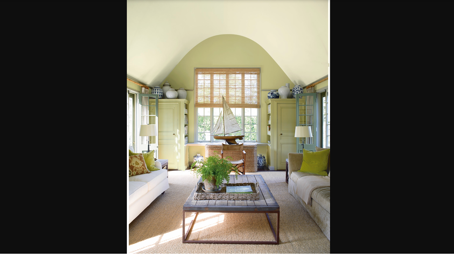 Deep olive green accent wall in a study with warm wood shelving, brass lighting, and a leather desk chair