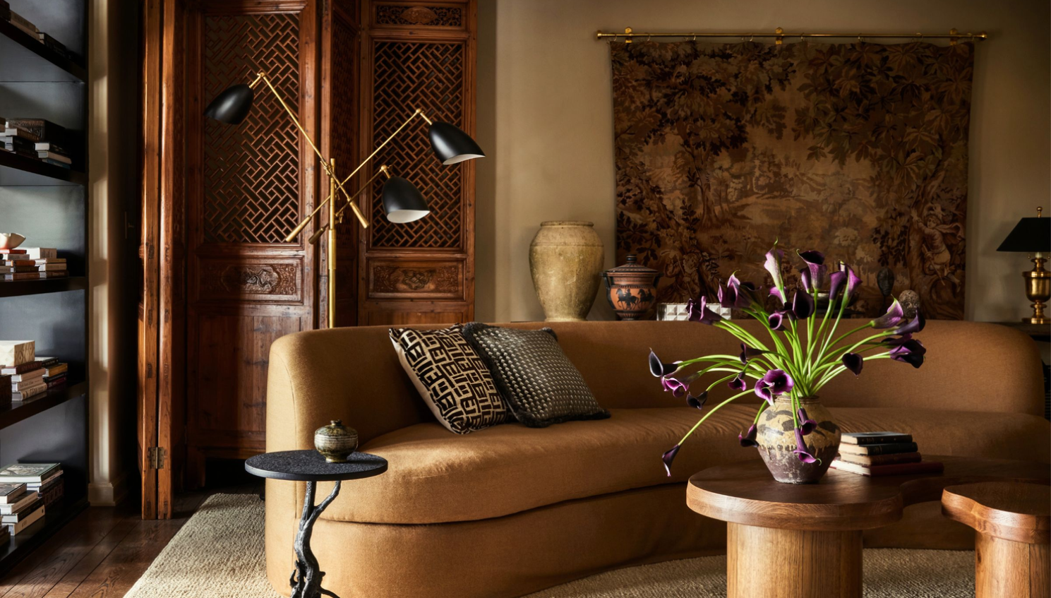 Chocolate brown accent wall behind a low-profile sofa with caramel leather, warm lighting, and textured neutral decor