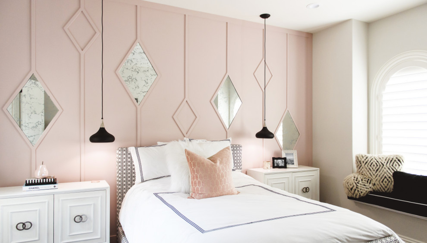 Soft clay pink bedroom accent wall behind a curved upholstered bed with warm white bedding and pale wood nightstands