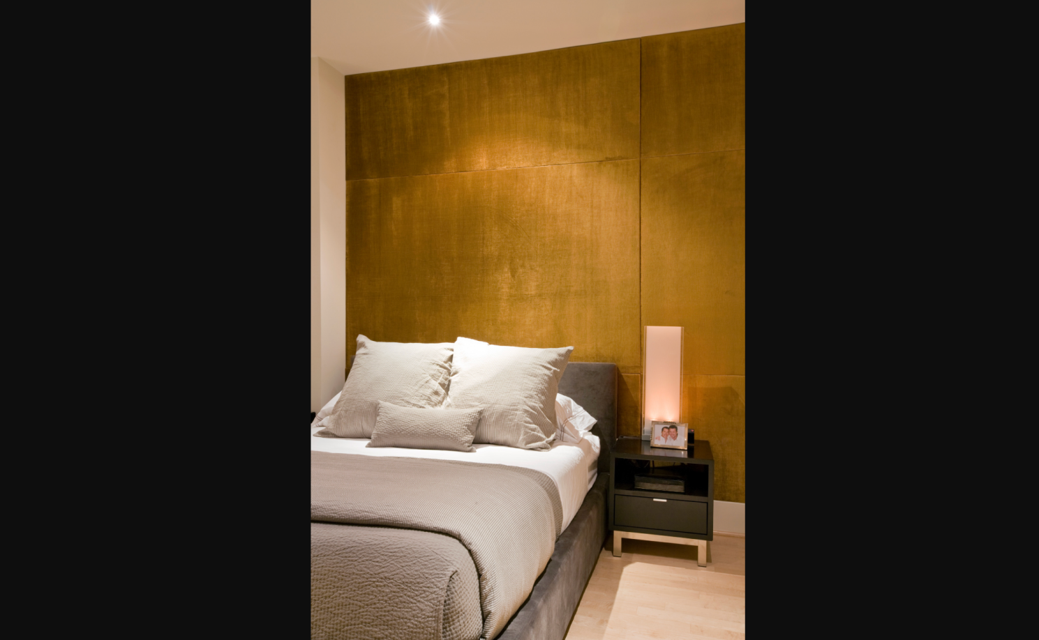 Upholstered fabric accent wall behind a bed with vertical panels, layered bedding, and warm bedside sconces