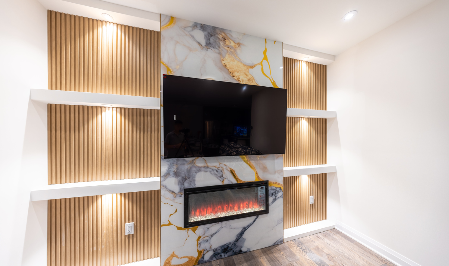 Fluted wall panel accent behind a TV with curved wood details, marble insert, and soft cove lighting