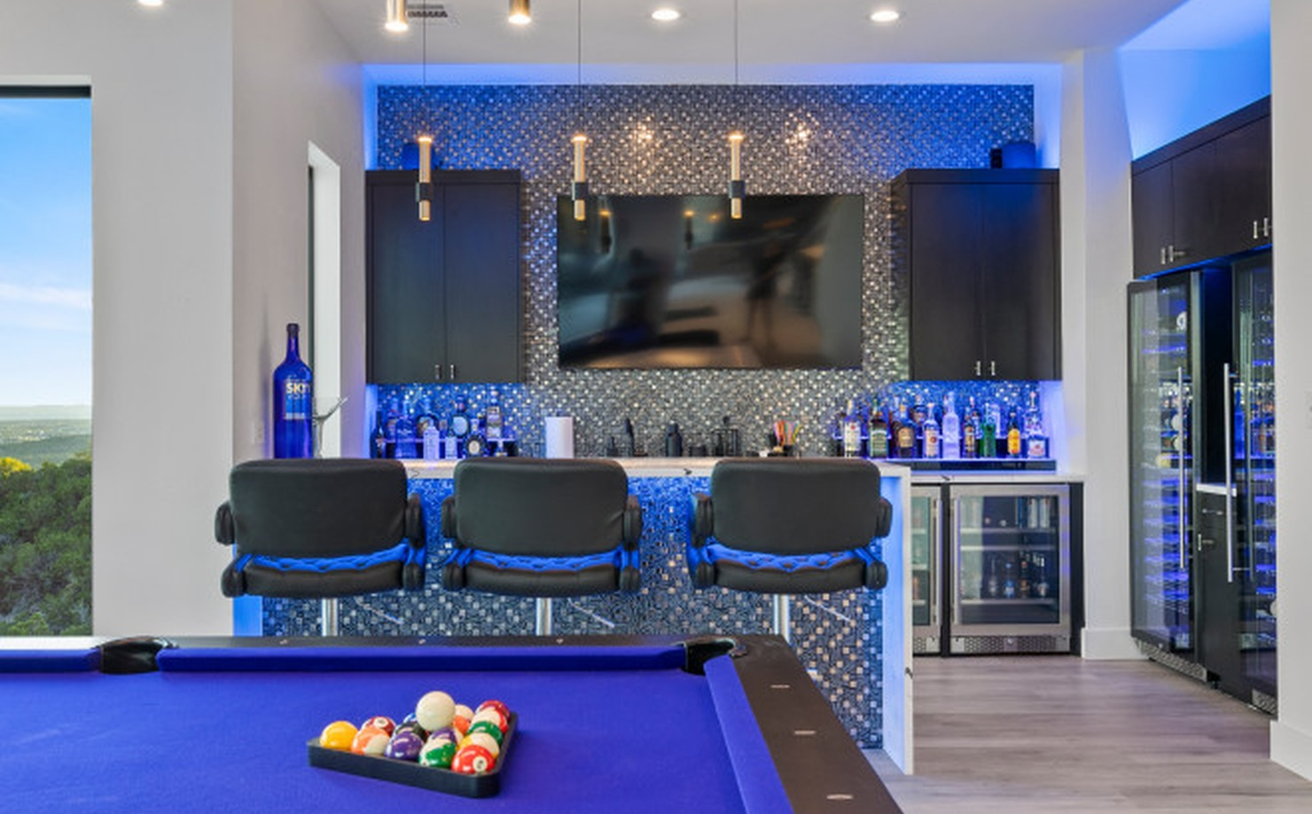 Sleek adult game room with pool table, custom bar, pendant lighting, and backlit mosaic tile