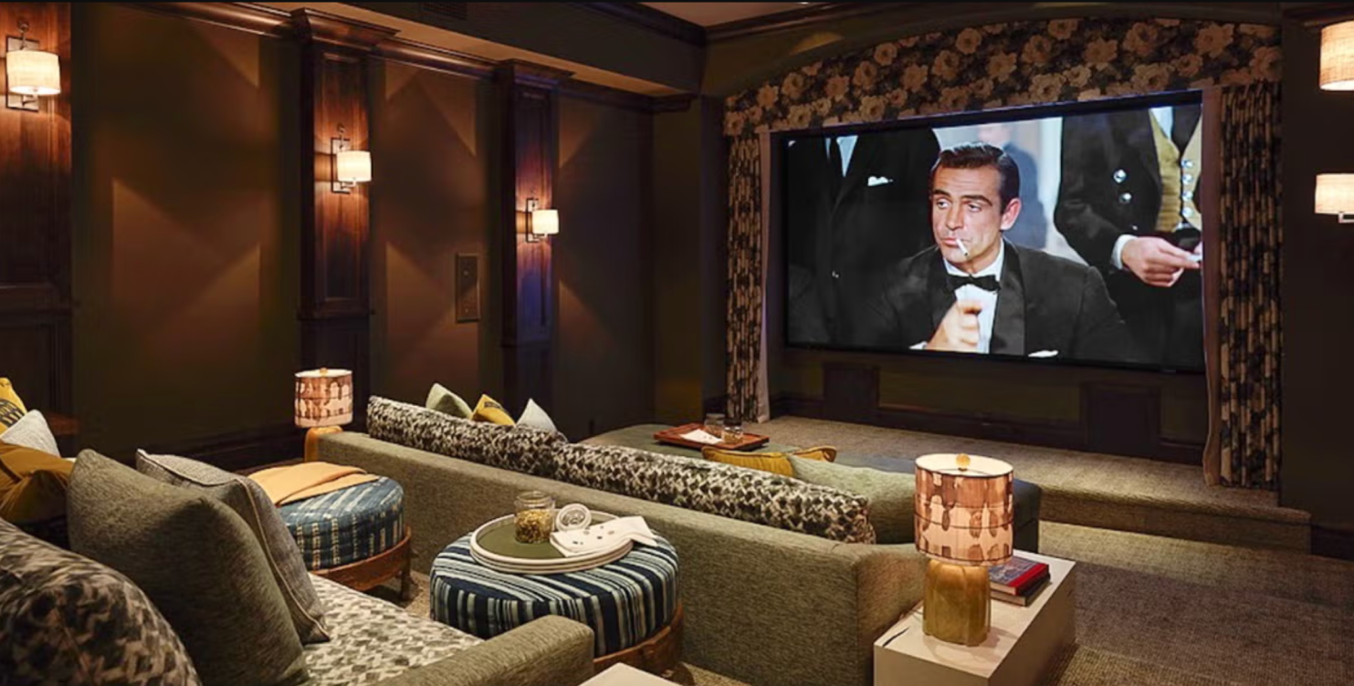 Modern home theater and game room with warm lighting, lounge seating, bar area, and cinematic mood
