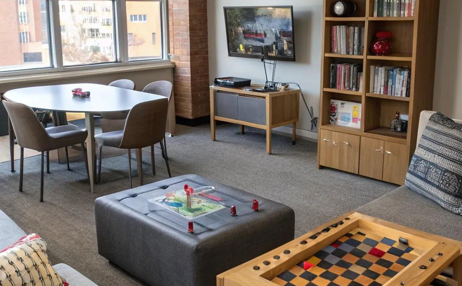 Apartment corner with rug, compact chairs, gaming shelf, wall decor, and small entertainment setup