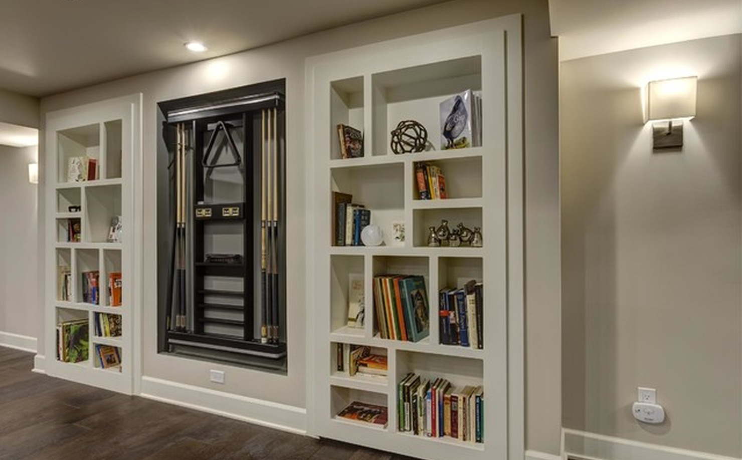 Game room with concealed bookshelf entrance, wall-mounted TV, dark wood floor, and traditional built-ins