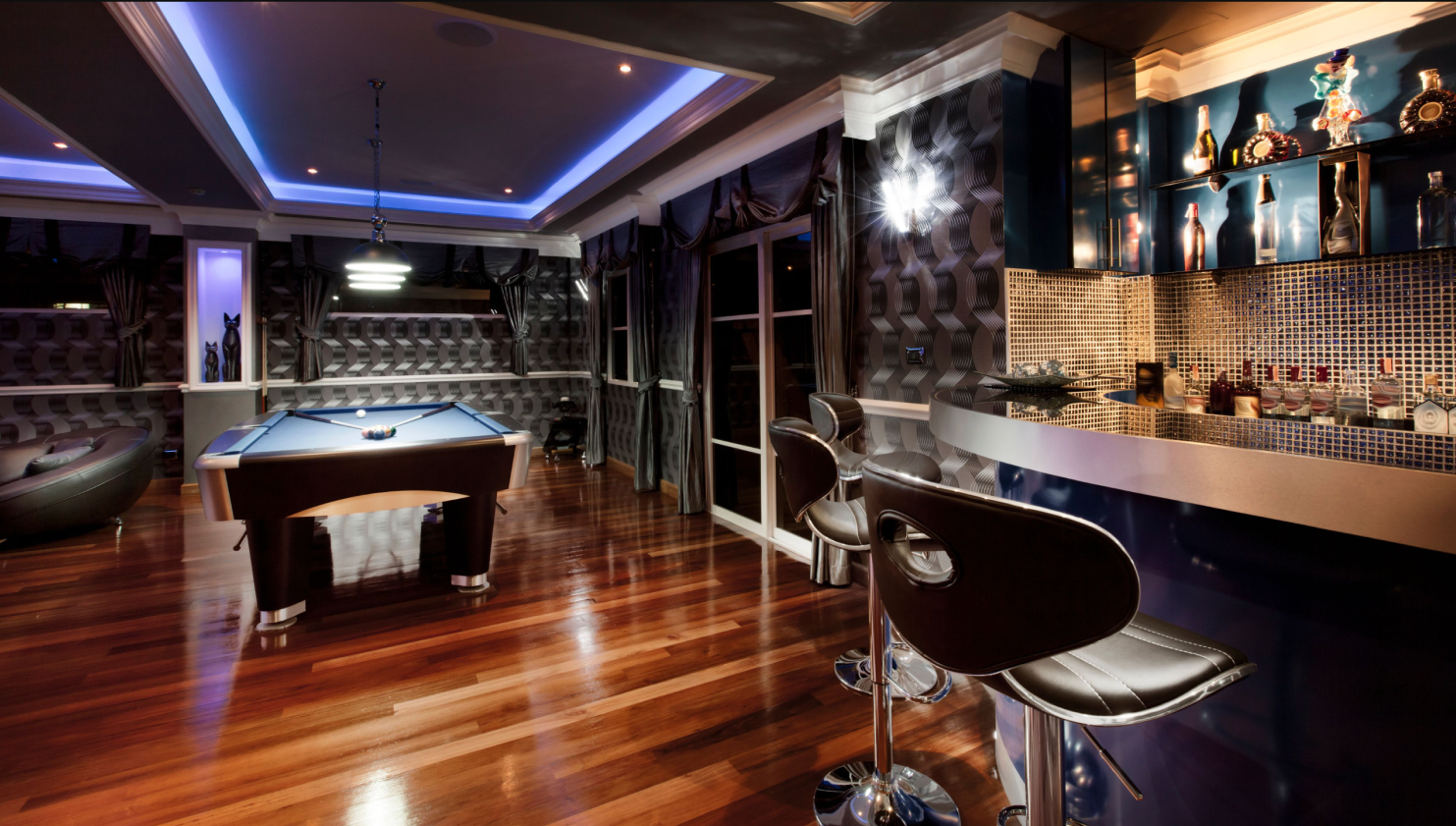 Upscale game room with pool table, custom bar, backlit tile, high ceilings and pendant lights