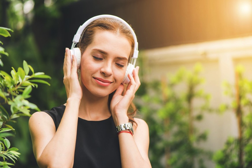 Woman smiling with her eyes closed with hands on her headphones