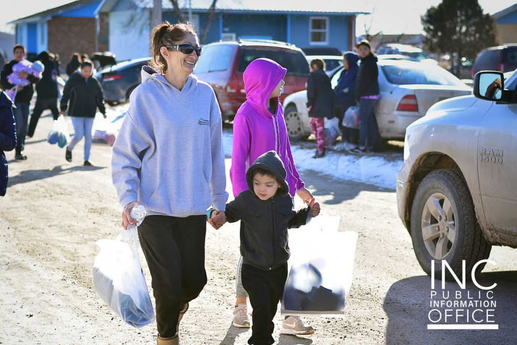 woman and children walking in the street carrying winter relief packages