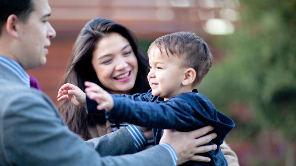 A family outdoors with their son’s outstretched arms to his dad.