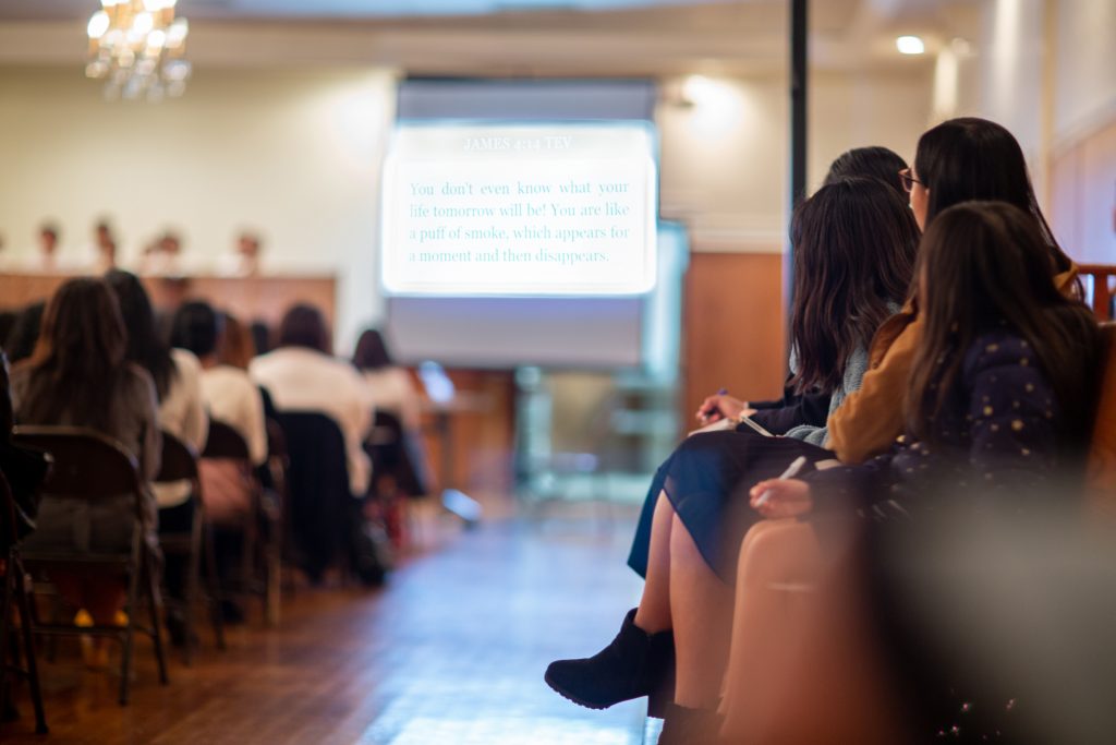 A worship service setting with a group of people looking at a screen holding a pen and paper.