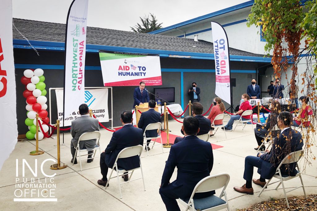 A small crowd sits on chairs far away from each other in a courtyard