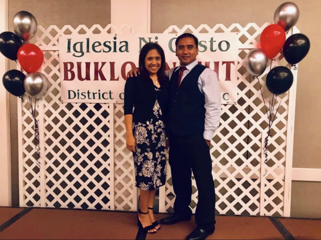 Couple smiling standing in front of an Iglesia Ni Cristo Buklod banner