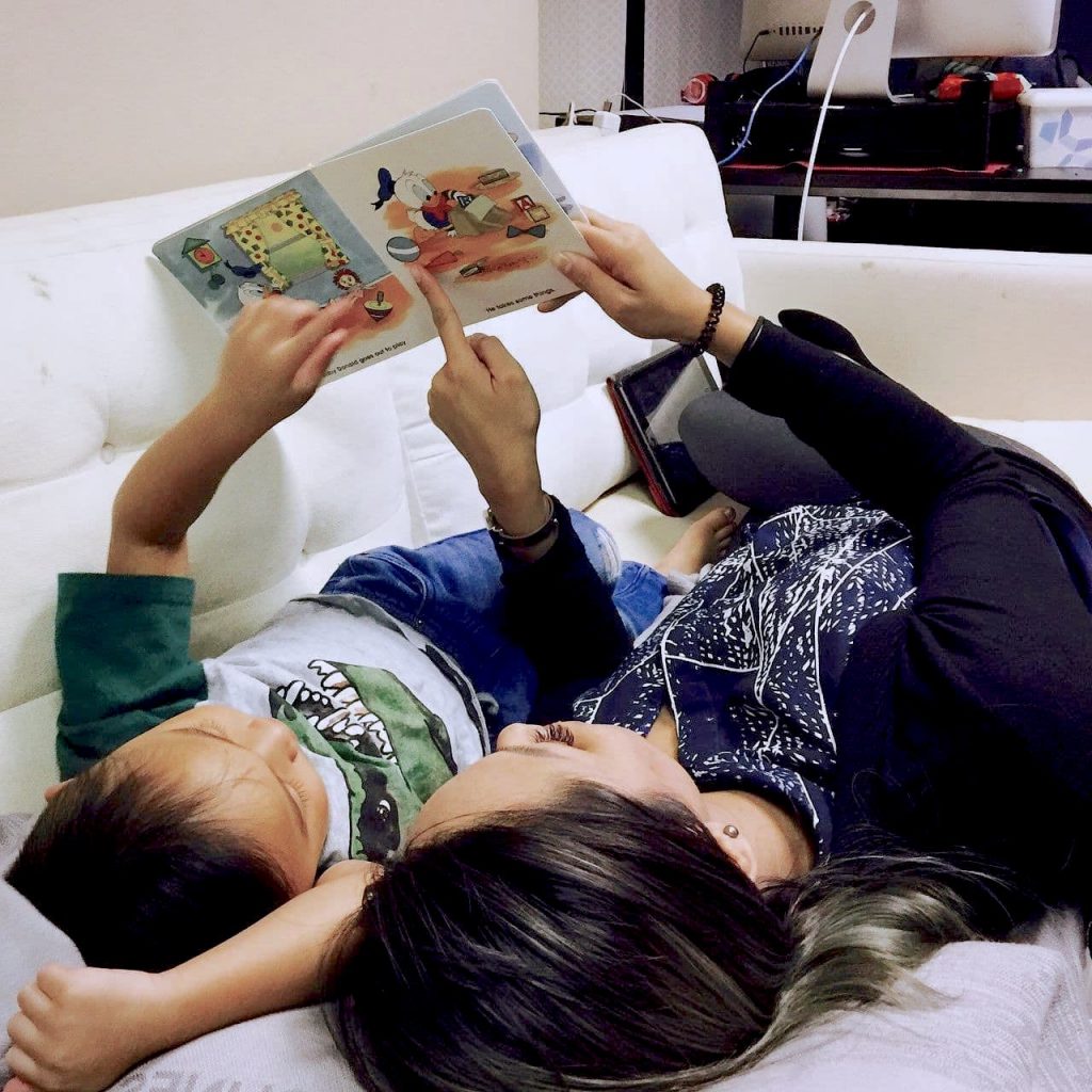 Mom and son reading a book lying down on couch.