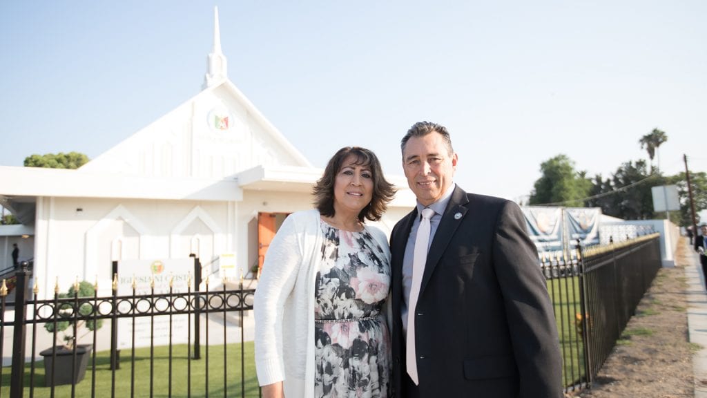 A couple smiling and standing in front of a house of worship.