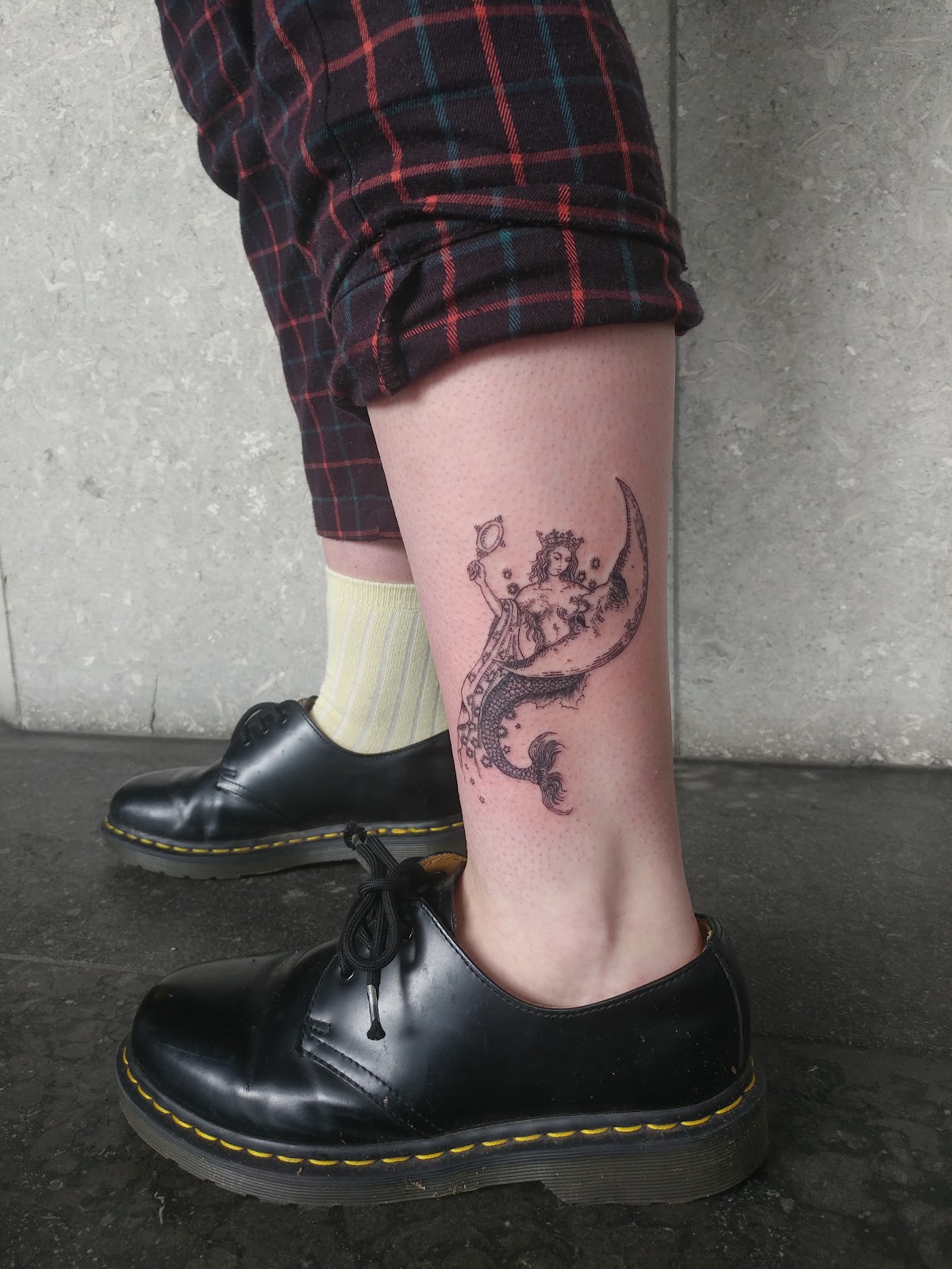 A detailed linework mermaid tattoo with a surreal eye and sun design on the ankle.