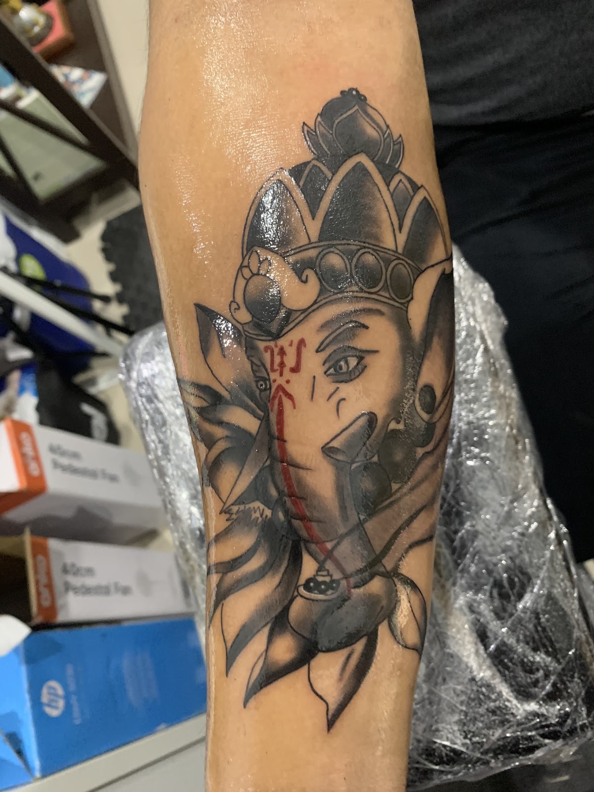 A detailed black and grey Ganesh tattoo with intricate floral details adorns the forearm.