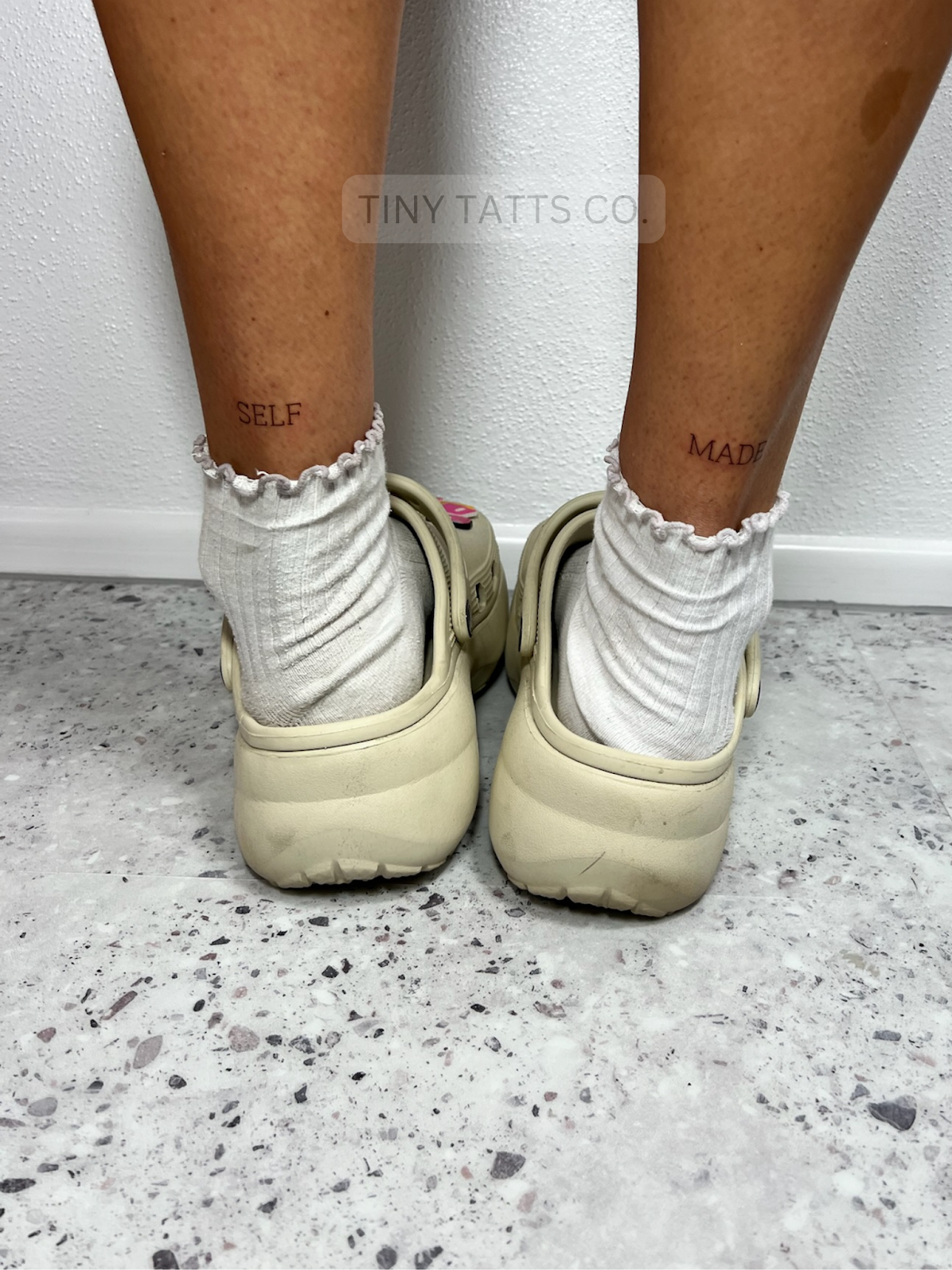 Close-up of minimalist 'SELF MADE' ankle tattoos.