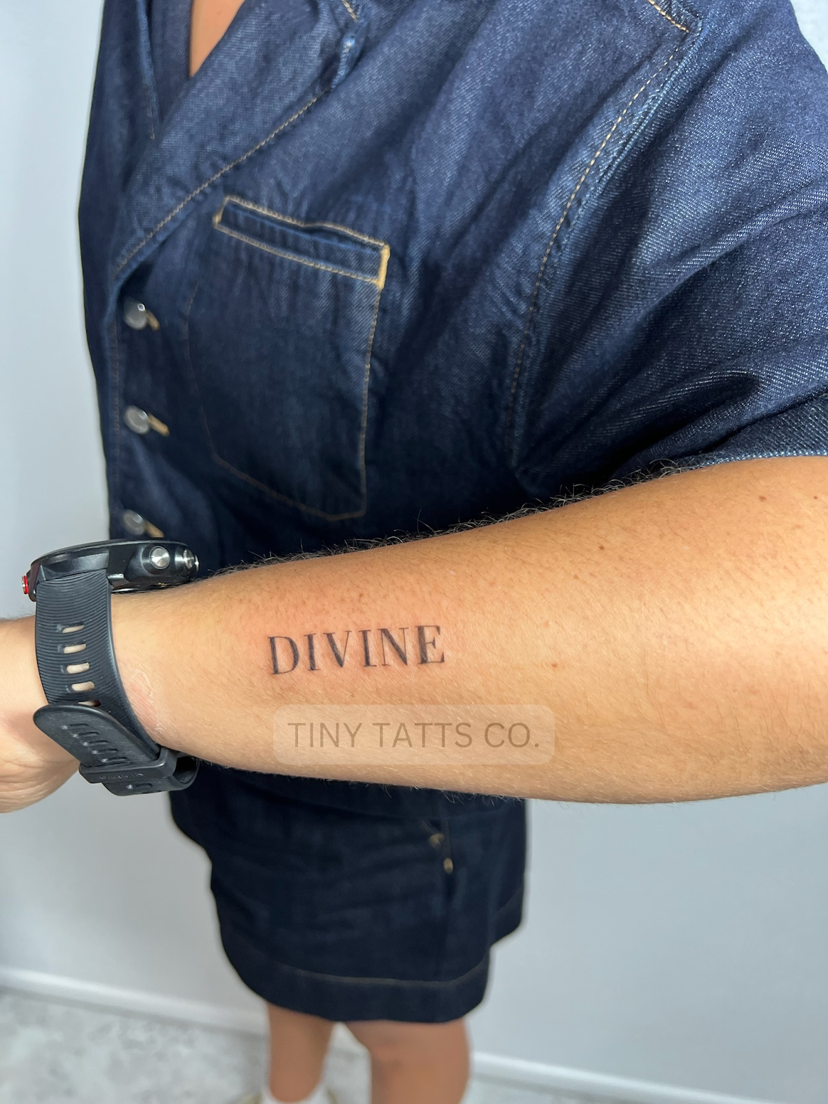 A close-up of a minimalist lettering tattoo on the forearm.