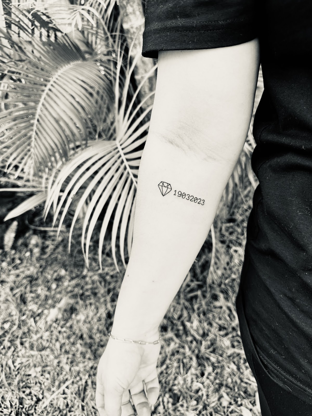 A simple linework diamond tattoo with a date on the forearm.