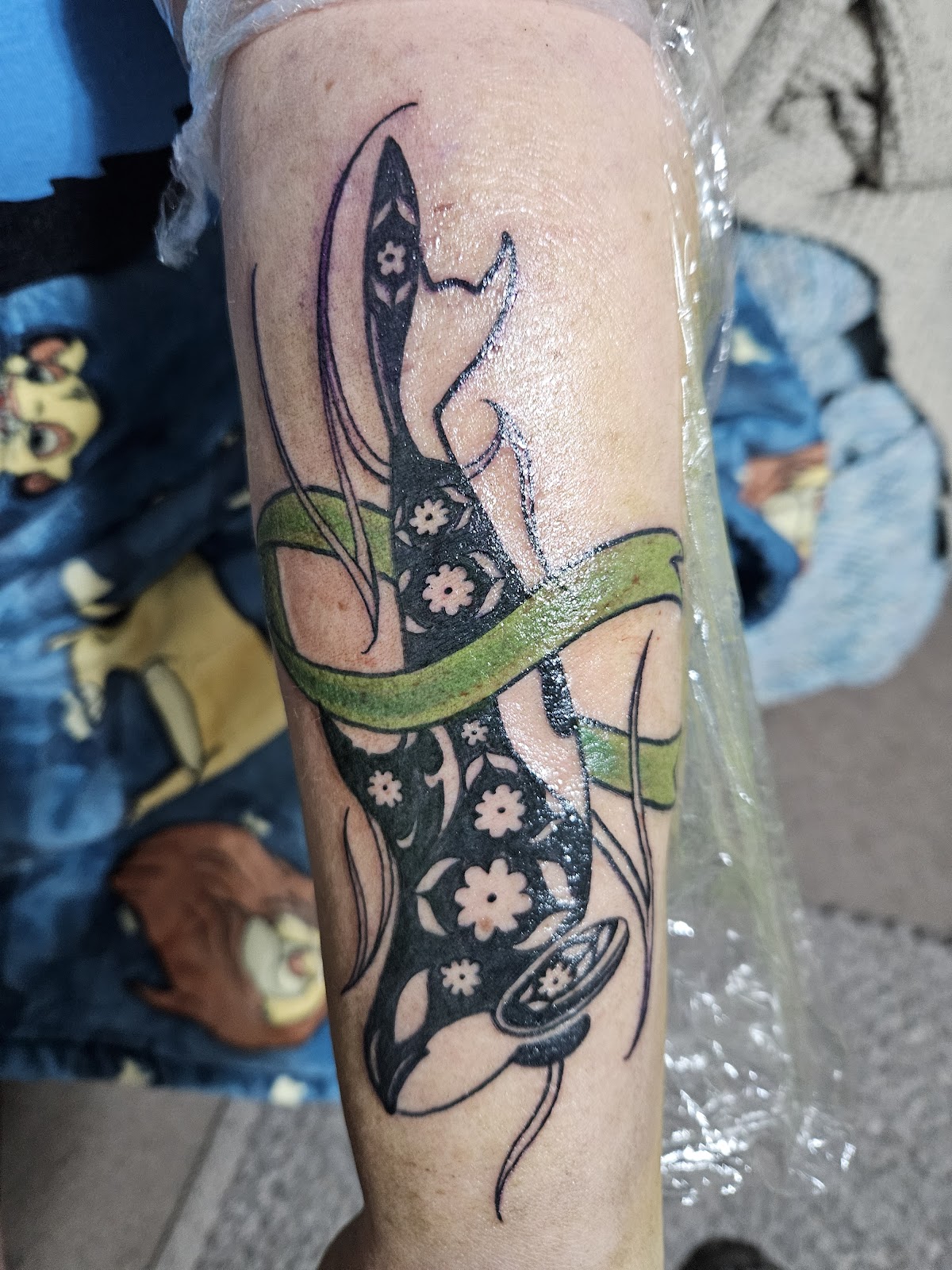 A whimsical illustrative tattoo featuring a cat and floral elements on the forearm.