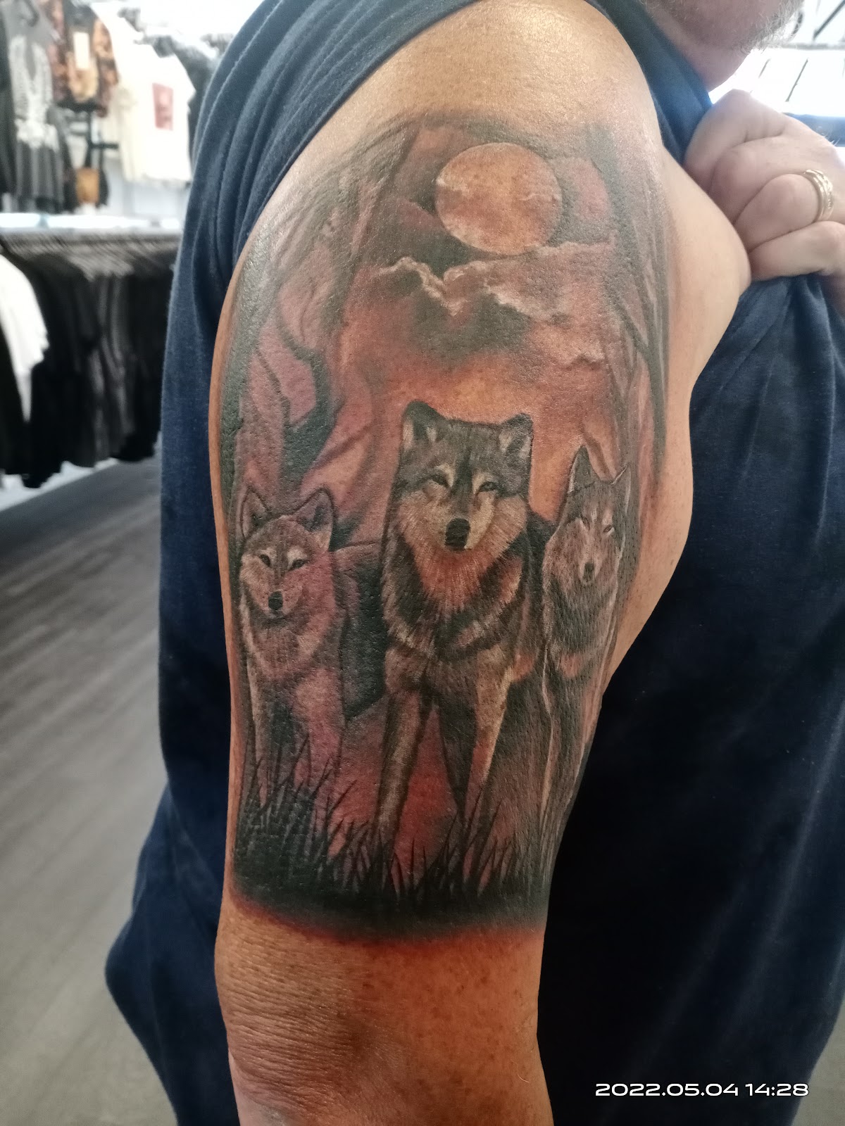 A detailed realism tattoo of three wolves howling at the moon.