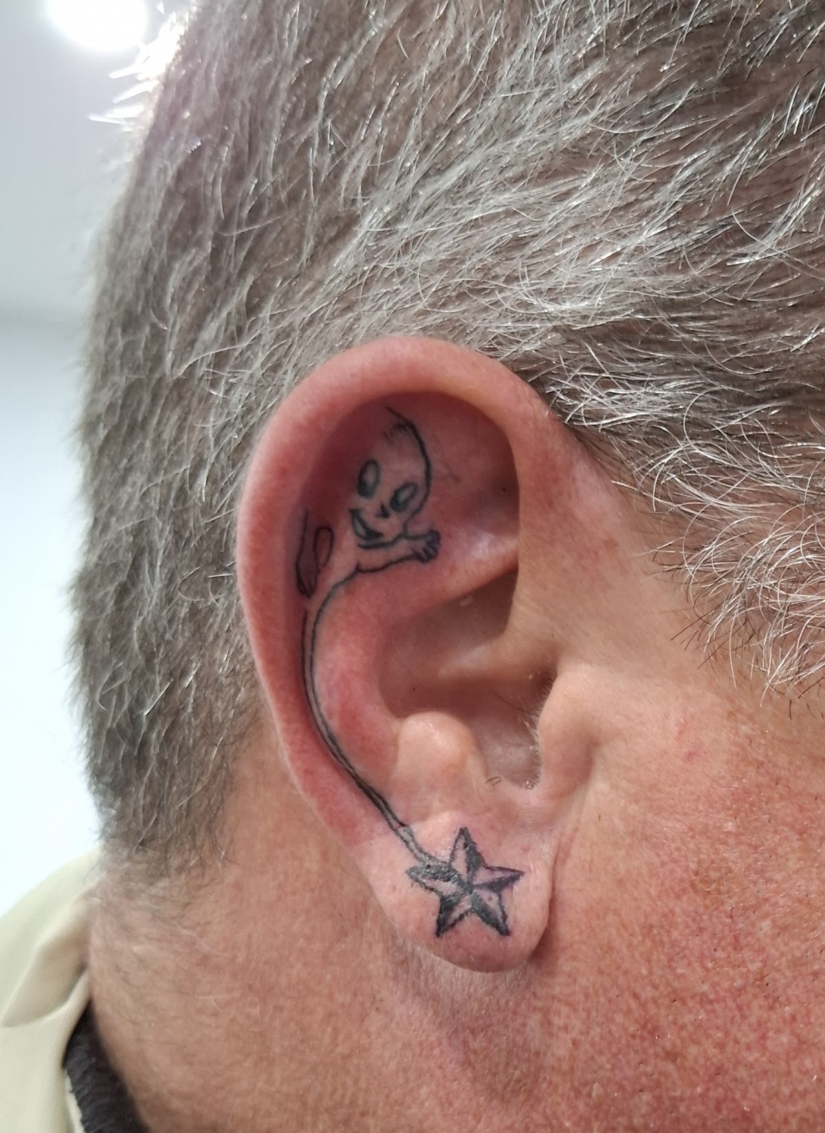 A playful linework tattoo featuring a cartoon eye and star on the ear.