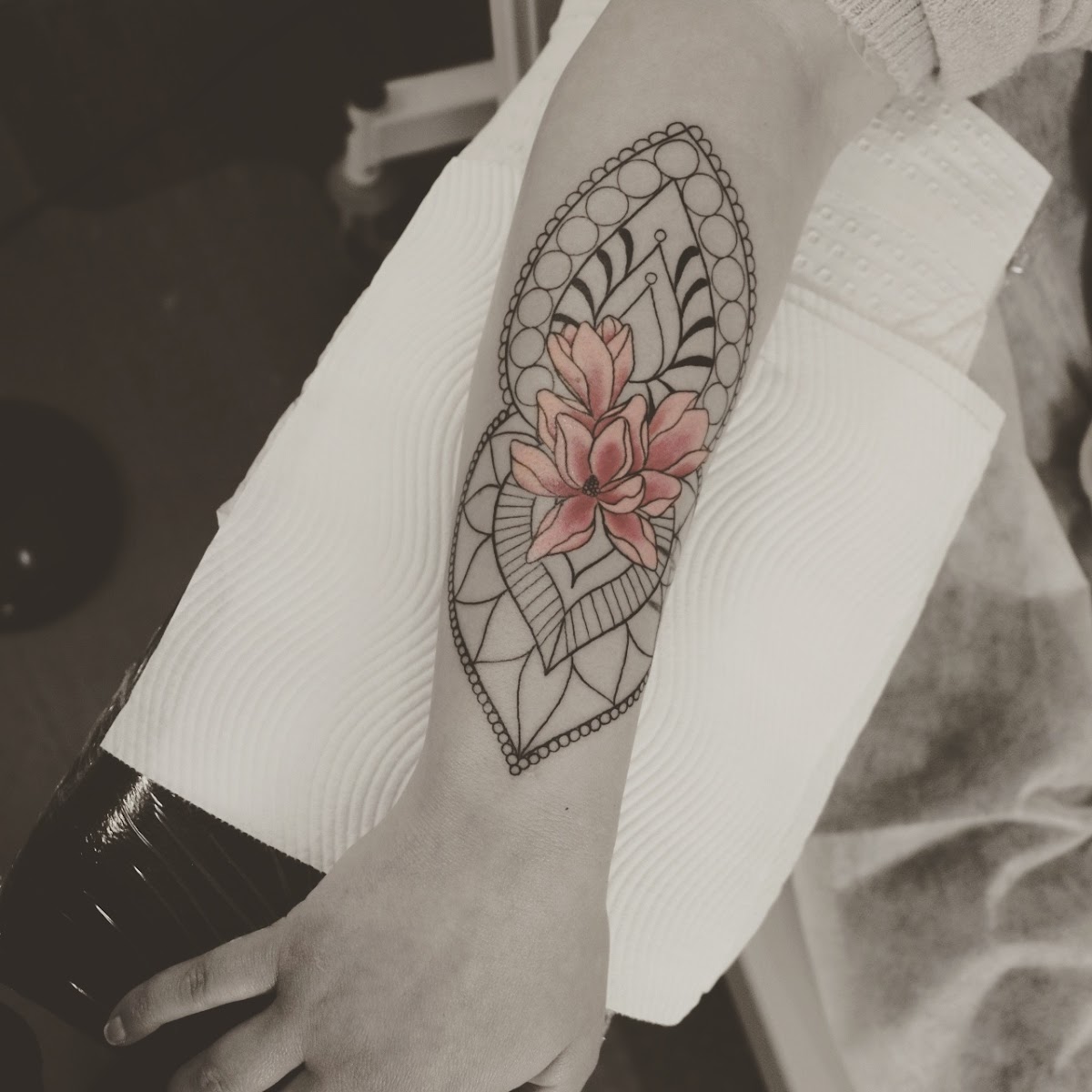 A detailed geometric lotus tattoo with dotwork shading adorns the forearm.