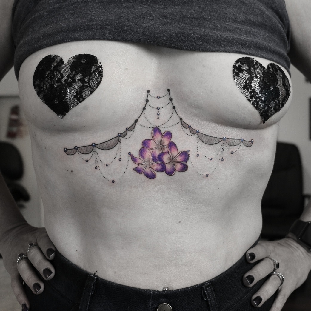A delicate floral tattoo with a lace-like design adorns the sternum.